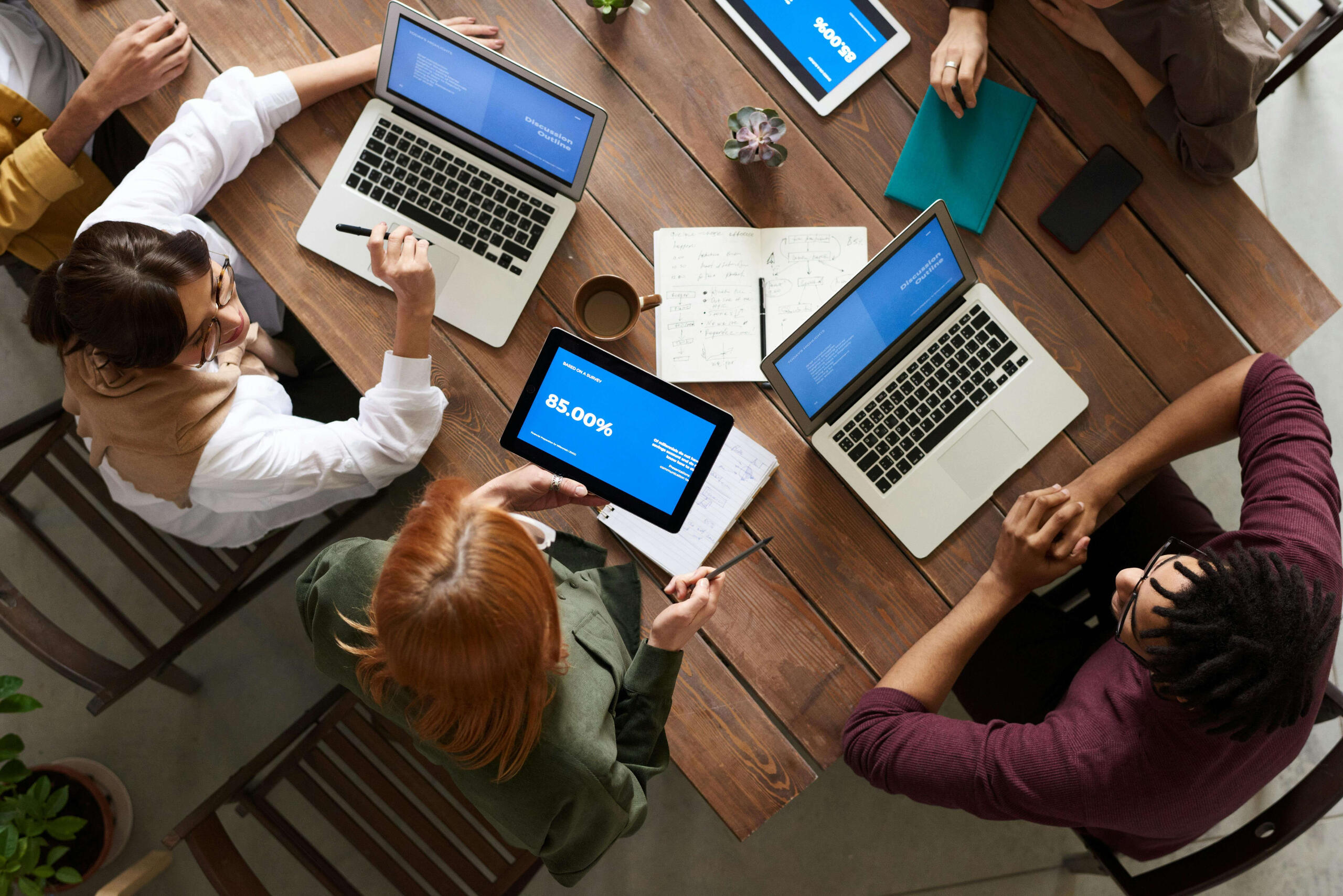A team of professionals sit around a desk working on laptops